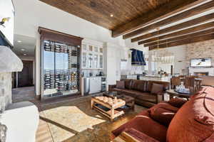 Living room with beverage cooler, a bar, beamed ceiling, and suspended lighting