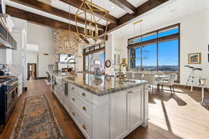 Kitchen featuring white cabinets, decorative light fixtures, dark stone counters, double oven range, and a large island