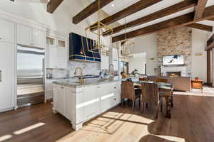 Kitchen with white cabinets, glass insert cabinets, stainless steel built in fridge, and dark wood finished floors