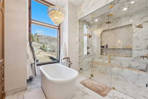 Bathroom with a marble finish shower, suspended lighting, a soaking tub, and light marble finish floors