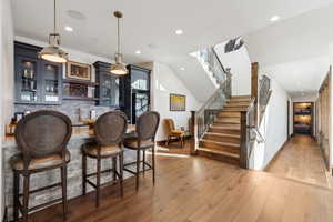 Indoor bar featuring glass fronted cabinets, light wood finished floors, pendant lighting, and backsplash