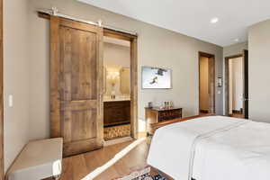 Bedroom with wood finished floors, connected bathroom, recessed lighting, and a barn door