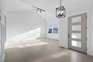 Foyer entrance with ceiling fan, light wood-style flooring, lofted ceiling, and suspended lighting