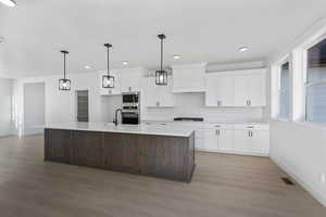 Kitchen featuring two tone color scheme, an island with sink, stainless steel appliances, decorative light fixtures, and light wood-style flooring