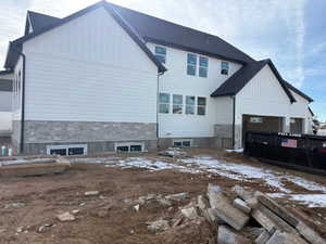 Snow covered back of property featuring board and batten siding and stone siding
