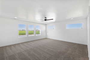Unfurnished room featuring dark carpet, a ceiling fan, and healthy amount of natural light