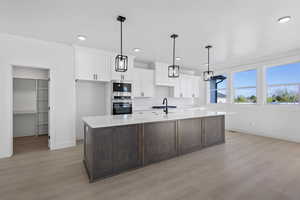 Two tone kitchen with two tone color scheme, light wood-style flooring, an island with sink, stainless steel appliances, and light stone counters