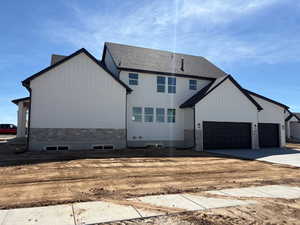 View of home's exterior featuring board and batten siding, concrete driveway, a garage, stone siding, and a shingled roof