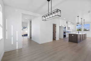 Dual tone kitchen featuring a center island with sink, pendant lighting, two tone color scheme, open floor plan, and light wood-type flooring