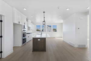 Kitchen with white cabinets, a center island with sink, open floor plan, light wood finished floors, and light stone countertops