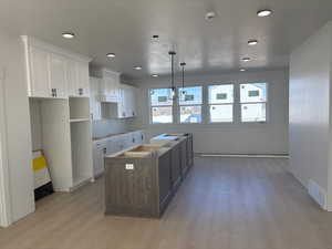 Dual tone kitchen featuring two tone cabinetry, a center island, light wood-style flooring, white cooktop, and decorative light fixtures