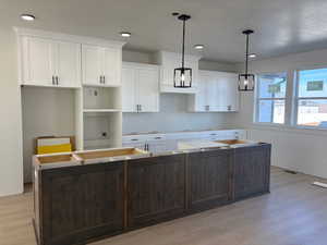 Dual tone kitchen featuring two tone cabinetry, a kitchen island, light wood-style flooring, and hanging light fixtures
