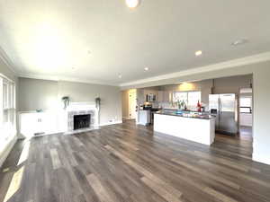 Spacious living room with wood burning fireplace, custom crown molding, dark wood-style flooring, recessed lighting, complete remodeled kitchen.