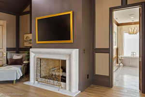 Detailed view of a fireplace with raised hearth, wood finished floors, ornamental molding, and hanging lights