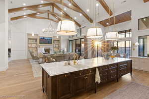 Two tone kitchen featuring a chandelier, light wood finished floors, light stone countertops, dual tone cabinets, and a kitchen island with sink