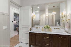Full bath featuring a wainscoted wall, double vanity, a decorative wall, curtained shower, and light wood finished floors