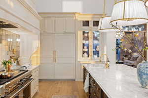 Kitchen with dual tone cabinets, double oven range, light stone countertops, light wood-type flooring, and glass fronted cabinets