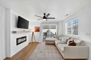 Living area featuring a textured ceiling, wood finished floors, a ceiling fan, and a glass covered fireplace