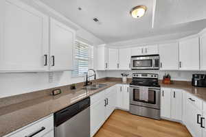 Kitchen with stainless steel appliances, white cabinets, dark stone countertops, light wood-style flooring, and a textured ceiling