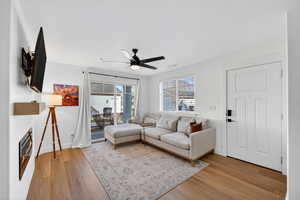 Living area featuring light wood finished floors, a glass covered fireplace, and ceiling fan
