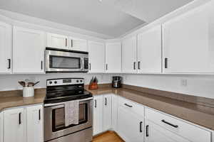 Kitchen featuring stainless steel appliances, white cabinetry, dark stone countertops, a textured ceiling, and light wood-style flooring