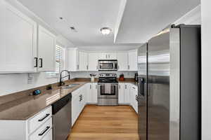 Kitchen featuring stainless steel appliances, white cabinets, dark stone counters, a textured ceiling, and light wood-style flooring