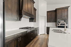 Gourmet kitchen cabinets in a dark wood tone, featuring light quartz countertops, a luxury gas range, and custom hood vent