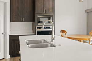 Gourmet kitchen cabinets in a dark wood tone, featuring light quartz countertops, a spacious island with sink, wall oven with microwave above, and semi formal dining area