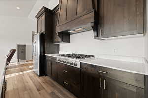 Gourmet kitchen cabinets in a dark wood tone, featuring light quartz countertops, a luxury gas range, and custom hood vent