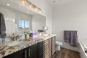 Primary en-suite bathroom featuring granite countertops, double sinks, dark wood cabinetry, and LVP flooring