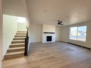 Unfurnished living room with a fireplace, light wood-type flooring, a textured ceiling, and ceiling fan