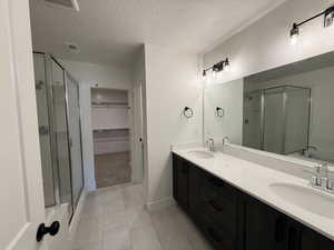 Full bath featuring a stall shower, a spacious closet, a textured ceiling, double vanity, and a tub to relax in