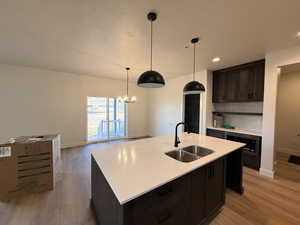 Kitchen featuring light wood-type flooring, dark wood finish cabinetry, a textured ceiling, a center island with sink, and suspended lighting