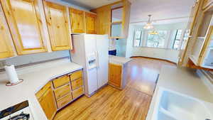 Kitchen featuring light wood-type flooring, light countertops, white appliances, hanging lights, and open floor plan