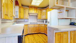 Kitchen with open shelves, light countertops, decorative backsplash, light wood-type flooring, and white refrigerator with ice dispenser