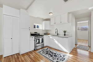 Kitchen featuring stainless steel gas range, white cabinetry, light countertops, white dishwasher, and light wood-style flooring
