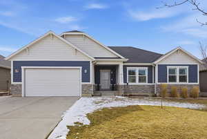 Craftsman-style house featuring stone siding, concrete driveway, a garage, and a yard