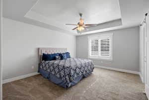Bedroom with a barn door, a tray ceiling, carpet floors, and ceiling fan
