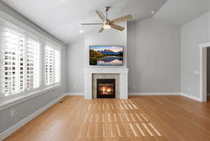 Unfurnished living room featuring lofted ceiling, light wood-style flooring, a tile fireplace, and a ceiling fan