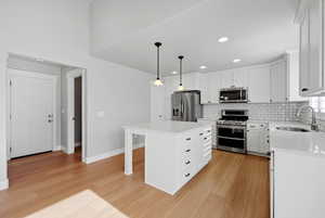 Kitchen featuring stainless steel appliances, white cabinetry, light stone countertops, a kitchen island, and light wood-style floors