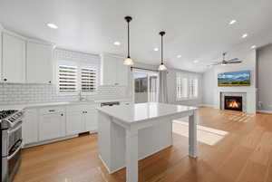 Kitchen featuring a glass covered fireplace, pendant lighting, range with two ovens, white cabinets, and light wood-style floors