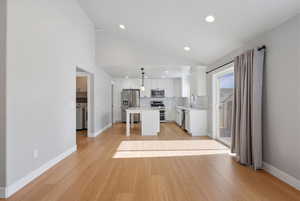 Kitchen featuring white cabinets, stainless steel appliances, decorative backsplash, decorative light fixtures, and a center island
