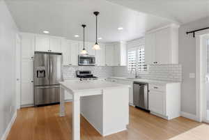 Kitchen with stainless steel appliances, hanging light fixtures, white cabinetry, and a breakfast bar