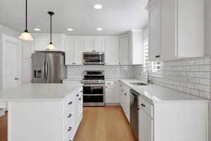 Kitchen featuring stainless steel appliances, light stone counters, white cabinetry, light wood finished floors, and decorative light fixtures