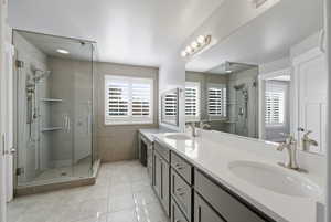 Full bathroom with double vanity, a stall shower, light tile patterned floors, and tile walls