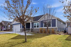 View of front of home with stone siding, a front yard, an attached garage, and driveway
