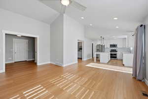 Unfurnished living room with vaulted ceiling, a ceiling fan, and light wood-type flooring