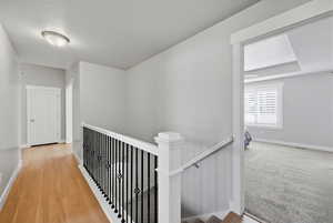 Corridor with an upstairs landing, light wood-style flooring, and a textured ceiling