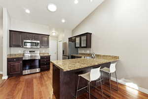 Kitchen with dark wood finish cabinetry, stainless steel appliances, a breakfast bar, a peninsula, and dark wood-style flooring