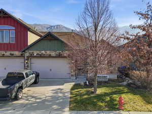 View of front of house with board and batten siding, stone siding, a mountain view, concrete driveway, and a front yard